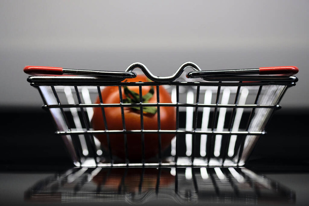 metal mini basket with tomato on a dark background with reflection - Foto, Imagen