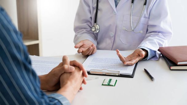 patiënt luistert aandachtig naar een mannelijke arts uitleggen van de symptomen van de patiënt of een vraag zoals ze papierwerk samen te in een overleg bespreken - Foto, afbeelding