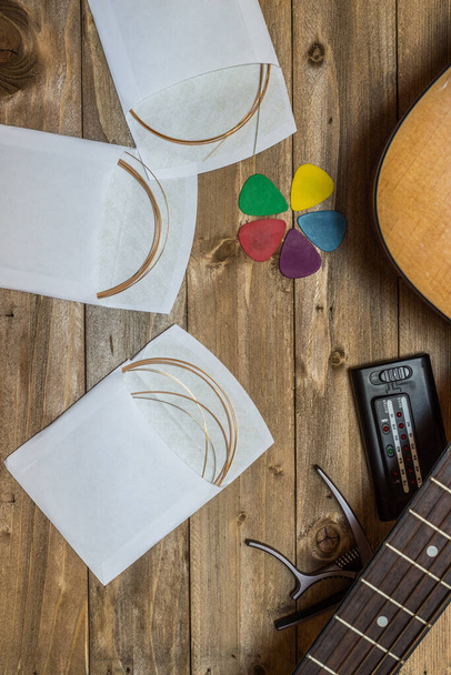 acoustic guitar and its accessories, strings, picks, capo, and tuner on wooden background - Photo, Image