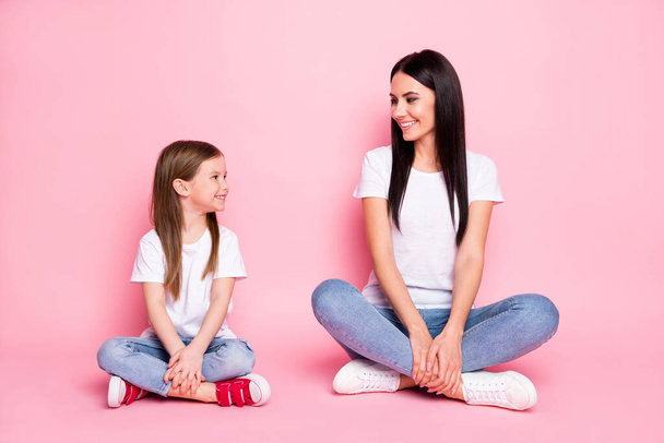 Full body photo of attractive young mom small daughter best friends sitting floor crossed legs look eyes wear casual white t-shirts jeans shoes isolated pastel pink color background - Foto, afbeelding