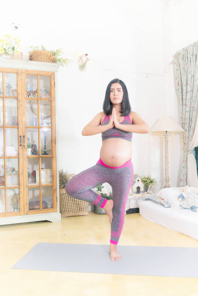 Terhes nő rózsaszín edzőruhát visel otthon. Edzés, jóga és fitness, terhesség koncepció. - Fotó, kép