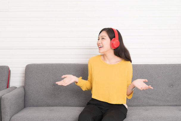 Piękna azjatycka kobieta długie włosy w żółtej koszuli z czerwonymi słuchawkami relaks na kanapie, słucha muzyki, chill out i koncepcji czasu wolnego. - Zdjęcie, obraz
