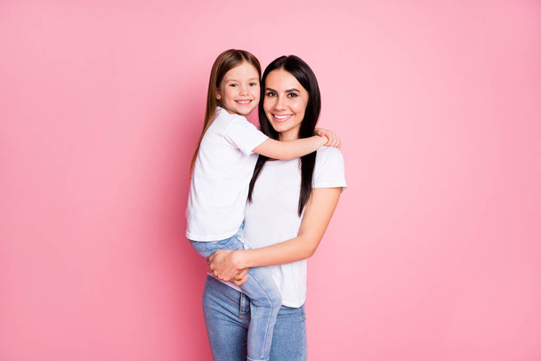 Photo of beautiful young mother hold arms little daughter two ladies hugging good mood best friends wear casual white t-shirts jeans isolated pastel pink color background - Foto, afbeelding