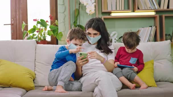 Sur le canapé-mère avec ses enfants portant le masque de protection, ils restent à la maison et utilisent le smartphone pour jouer à un jeu le petit garçon ne porte pas le masque de protection temps de quarantaine nouveau Coronavirus 2019
 - Séquence, vidéo