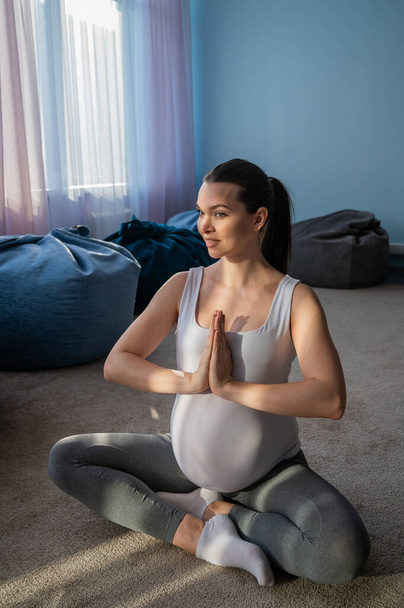 Pregnant woman smiles in yoga practice. A woman in the third trimester leads Pilates. Classes to prepare for childbirth. Waiting for the baby. Namaste - Fotografie, Obrázek