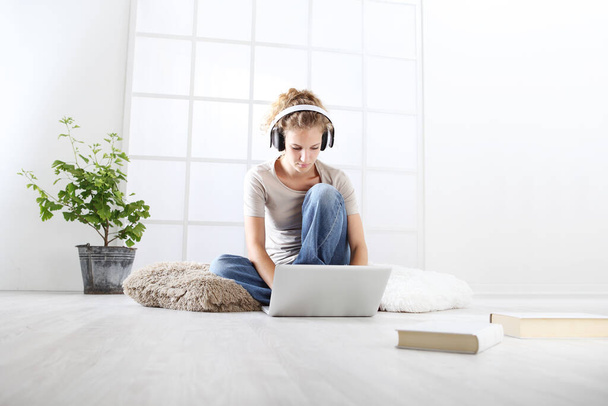 mujer joven sentada en la sala de estar estudiando con auriculares y computadora, quedarse en el concepto de casa - Foto, imagen