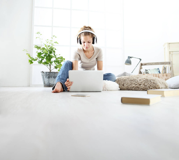 junge Frau sitzt im Wohnzimmer und lernt mit Kopfhörer und Computer, bleibt zu Hause - Foto, Bild