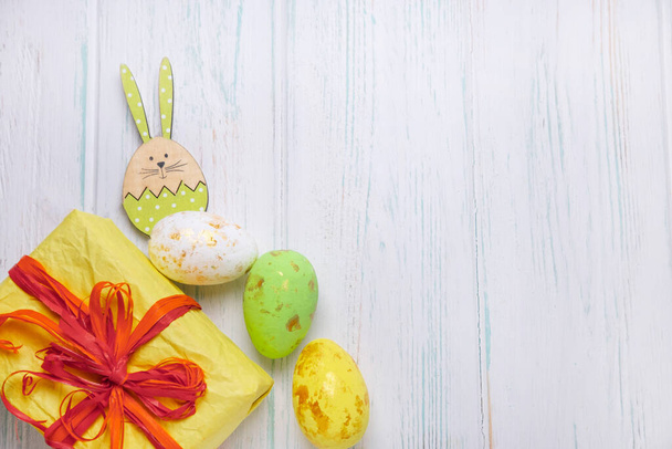 Easter backgrounds for greeting lettering, promotions. Gift box and easter eggs on a light wooden background with figures of wooden rabbits. - Foto, Imagen