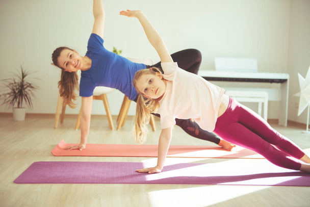 Pretty young woman with her adorable teenager daughter practicing yoga at home during coronavirus quarantine - Foto, immagini