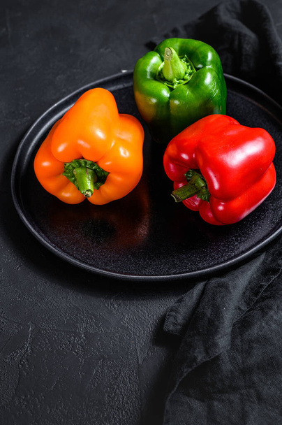 Green, orange and red bell peppers on a plate. Black background. Top view. - Fotó, kép