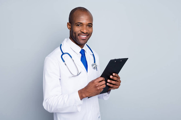 Photo of family doctor dark skin guy cheerful beaming smiling patient hold clipboard read prescription test results wear lab coat neck tie stethoscope isolated grey color background - Fotó, kép