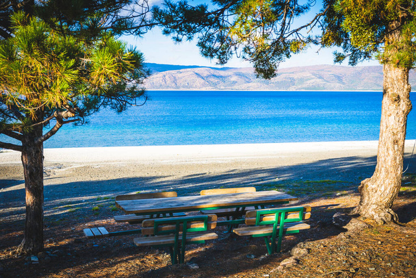 Spokojny widok na błękitne jezioro Salda w tle i stoły otoczony sosnami na pierwszym planie. Wakacje letnie i pknik nad jeziorem w Turcji.2020 - Zdjęcie, obraz