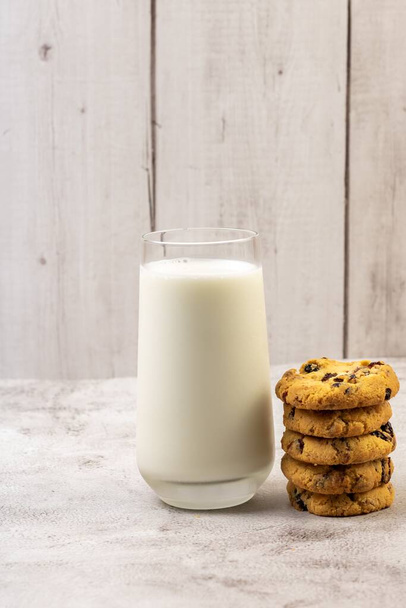 A vertical shot of a pile of chocolate chip cookie beside a glass of milk on a table - Foto, imagen