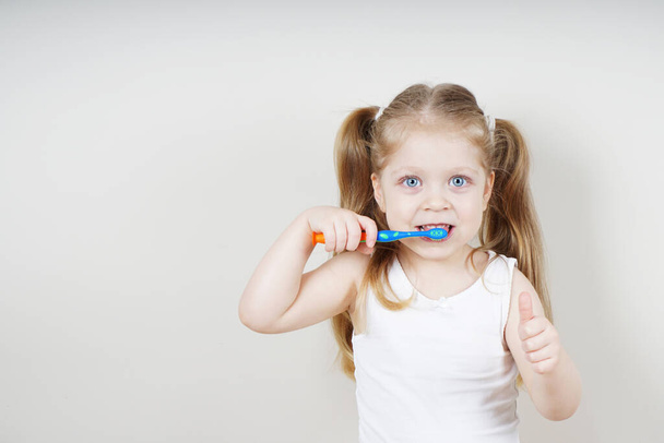 A little girl of European appearance brushes her teeth on a light background. The concept of healthy teeth. Dentistry - Fotó, kép