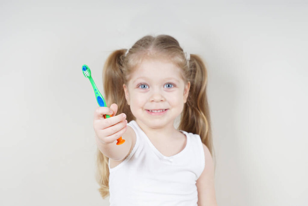 A little girl of European appearance brushes her teeth on a light background. The concept of healthy teeth. Dentistry - Photo, Image
