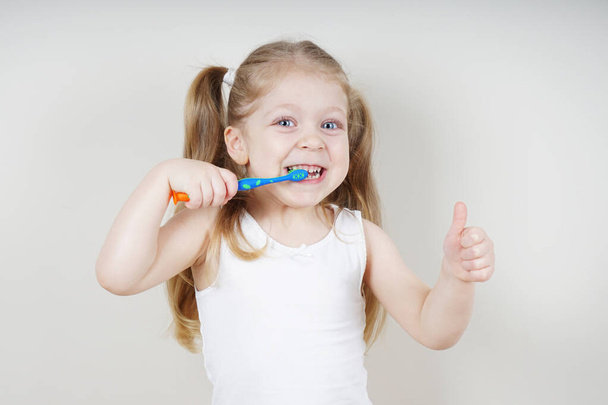 A little girl of European appearance brushes her teeth on a light background. The concept of healthy teeth. Dentistry - Fotoğraf, Görsel
