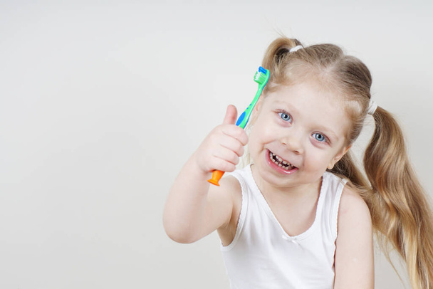 Avrupalı görünümlü küçük bir kız arka planda dişlerini fırçalıyor. Sağlıklı diş kavramı. Dişçilik - Fotoğraf, Görsel