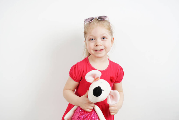 Photoshoot of a little beautiful girl in sunglasses, in a pink fuchsia color dance. With a soft toy in his hands. On an isolated background for advertising - Fotó, kép