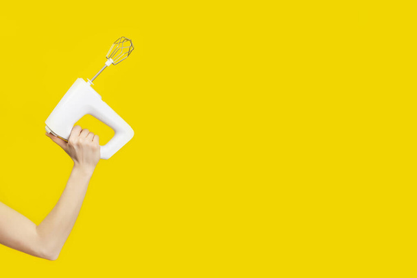 Misturador de cozinha branca na mão feminina isolado no fundo amarelo brilhante. Espaço para cópia. Conceito de cozinha moderna
 - Foto, Imagem