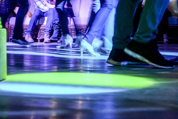 Bela vista e cena nos pés, sapatos de pessoas dançando, jovens em um clube ou bar em um fundo escuro com iluminação
. - Foto, Imagem