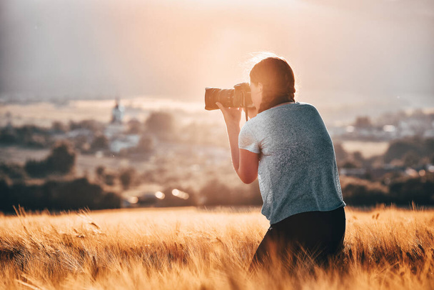 Νεαρό κορίτσι λήψη φωτογραφιών με επαγγελματική κάμερα στη φύση καλοκαίρι χρυσό χωράφι σίκαλης - Φωτογραφία, εικόνα