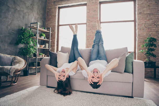Portrait of attractive lovely foolish childish comic cheerful cheery glad crazy playful couple lying on divan showing ok sing like glasses staying at modern industrial loft style brick interior house - Фото, изображение