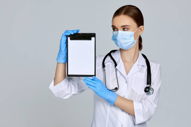 woman doctor in mask and rubber gloves and with stethoscope holding clipboard - Foto, immagini