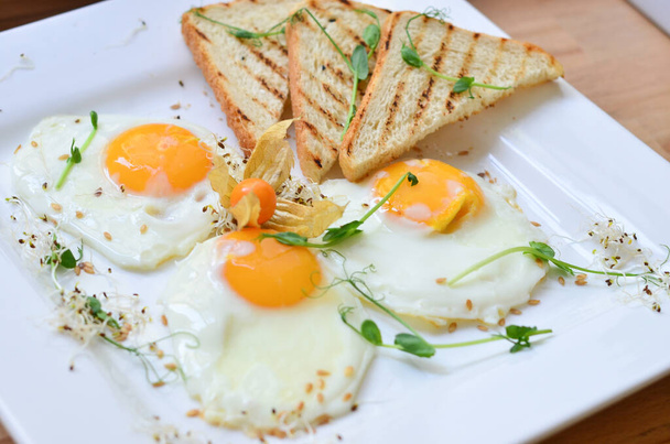 śniadanie dwóch jajek warzyw, pomidorów, grochu, orzechów i zieleni z sosem, tosty ze śmieciami na białej talerzu z urządzeniami - Zdjęcie, obraz