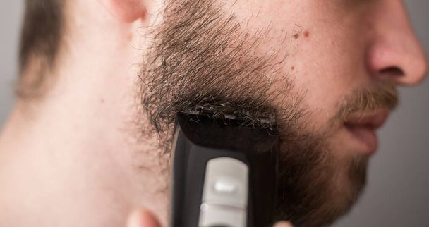 Man shaves his beard with an electric razor - Fotó, kép