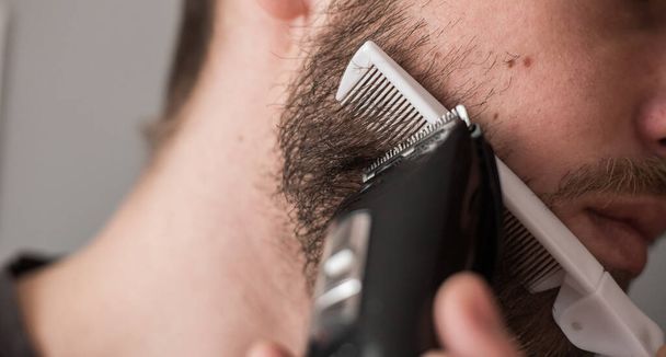 Man shaves his beard with an electric razor - Фото, изображение