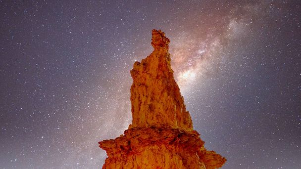 Galáxia no céu noturno sobre a estátua natural da Rainha Vitória criada pela erosão de um Pináculo de Arenito no Jardim da Rainha parte do Parque Nacional Bryce Canyon, Utah, Estados Unidos
 - Foto, Imagem