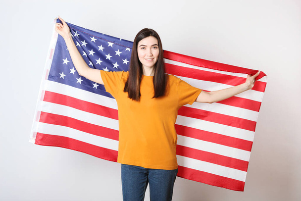 Beautiful young girl holding the flag of America on a colored background. - Foto, immagini