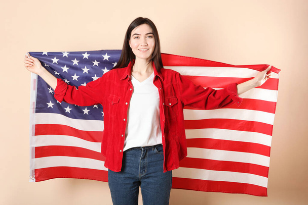 Όμορφη νεαρή κοπέλα που κρατά τη σημαία της Αμερικής σε έγχρωμο φόντο. - Φωτογραφία, εικόνα