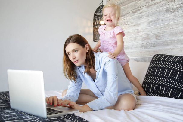 Werk vanuit huis met een kleintje. Jonge moeder probeert te werken op de laptop tijdens het oppassen. Stressvolle moeder probeert te multitasken.  - Foto, afbeelding