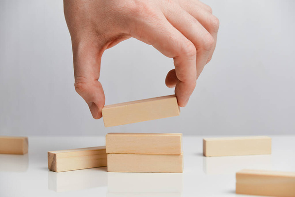Concept of rebuilding a business after bankruptcy. Hand holds wooden blocks on a white background. Close up. - Photo, Image