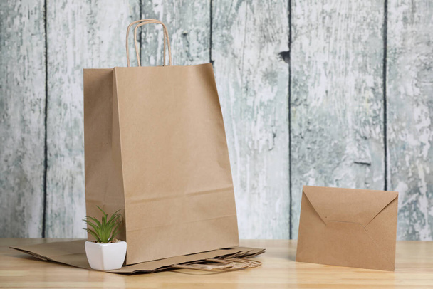 Bolsa de compras de papel reciclado, sobre y planta verde en una maceta blanca sobre un fondo de madera. Producto ecológico
. - Foto, Imagen