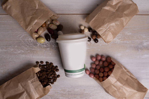 Dřevěné pozadí s jednorázové papírové šálek kávy, čokoládové bonbóny a kávová zrna - Fotografie, Obrázek