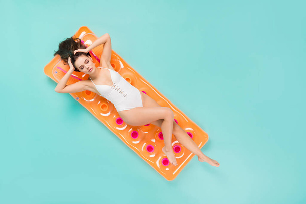 Full length high angle above flat lay view photo of beautiful lady lying swimming big mattress relaxing arms touch hairdo head wear bodysuit isolated pastel teal color background - 写真・画像