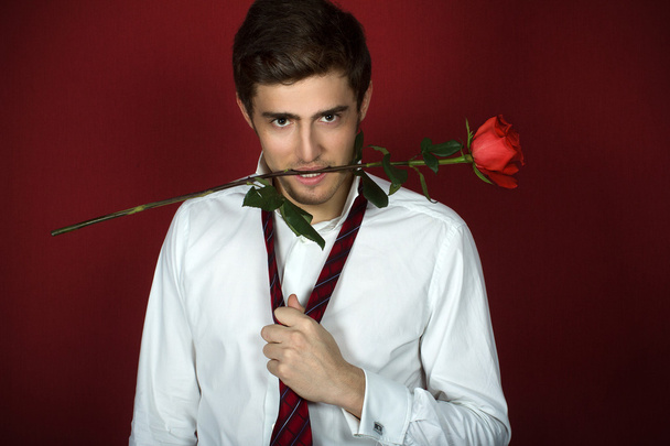 Beautiful young man holds a rose with teeth - Фото, изображение