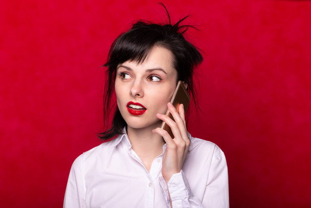 manager girl in a white shirt speaks on the phone, red background - Fotografie, Obrázek
