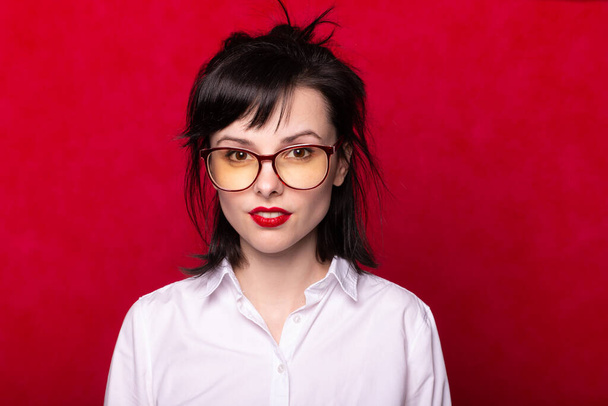 chica en una camisa blanca y gafas con labios rojos, fondo rojo
 - Foto, Imagen