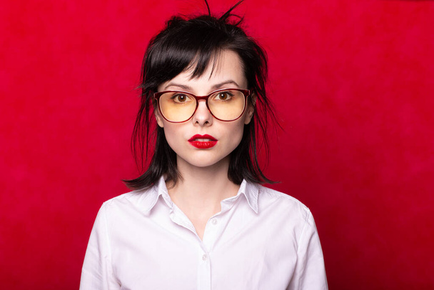girl in a white shirt and glasses with red lips, red background - Foto, imagen