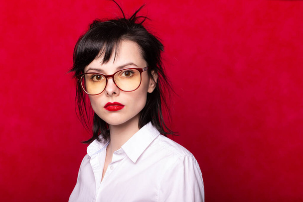menina em uma camisa branca e óculos com lábios vermelhos, fundo vermelho
 - Foto, Imagem