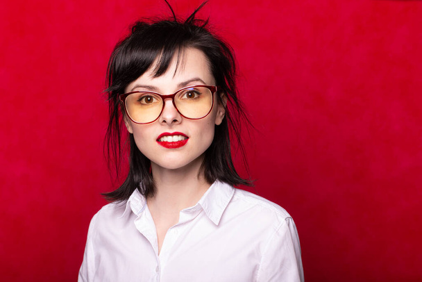 lány egy fehér ing és szemüveg piros ajkak, piros háttér - Fotó, kép