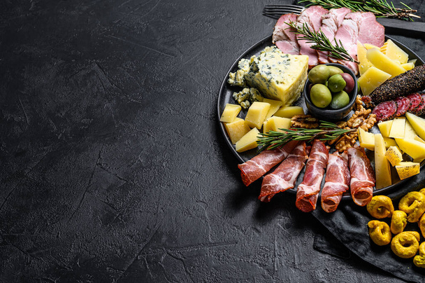 Typical italian antipasto with prosciutto, ham, cheese and olives. Black background. Top view. Space for text. - Zdjęcie, obraz