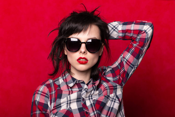 girl in a plaid shirt and sunglasses, red background - Fotó, kép