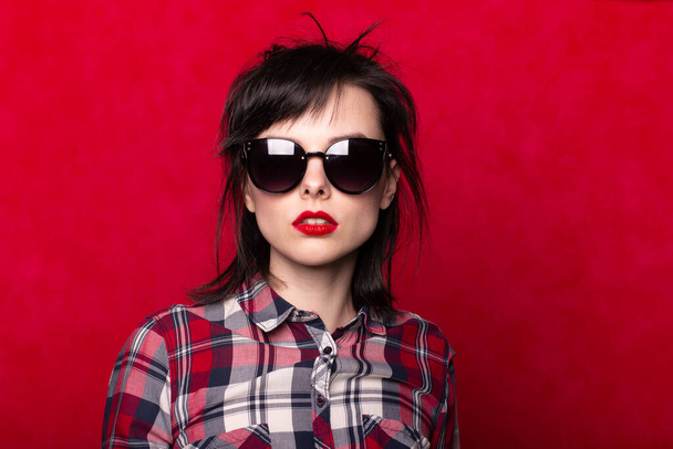 girl in a plaid shirt and sunglasses, red background - Foto, Imagem