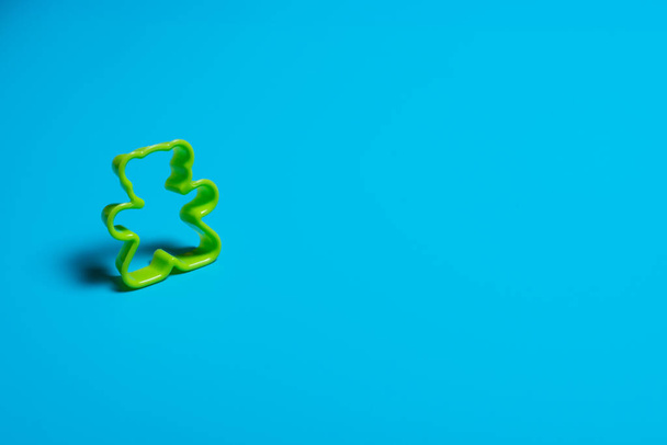 Green plastic cookie cutter for making cookies in the shape of a teddy bear on a blue background. Culinary concept. Flat lay with copyspace. - Фото, зображення
