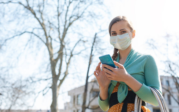Woman using her phone wearing mask reading news about Covid-19 - Foto, Imagen