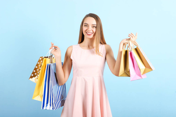 Beautiful young girl with paper bags for shopping on a colored background - Foto, imagen